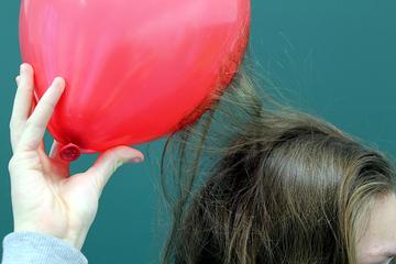 Воздушный шарик, потёртый о волосы, поднесён к голове: пряди тянутся к нему